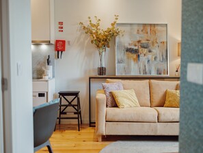 A living room with a sofa, a small table, a vase with dried flowers, and a painting on the wall. - Apartment  by Interhome (Porto)