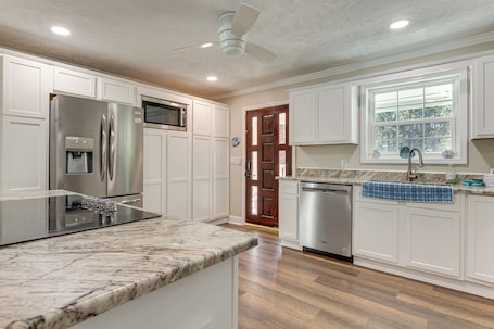 A kitchen with white cabinetry, a stainless steel refrigerator, a dishwasher, and a marble countertop.