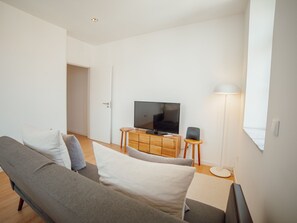 Una sala de estar moderna con un sofá gris, un televisor de pantalla plana sobre un mueble de madera y una lámpara de pie.