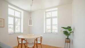 Ett rum med ett runt träbord och stolar, stora fönster, en hängande lampa och en krukväxt.