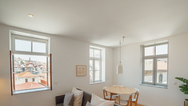 Ett modernt vardagsrum med en soffa, ett matbord och stora fönster med utsikt över staden.