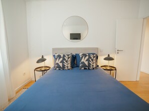 Ein Schlafzimmer mit einem Bett, zwei Nachttischen, einem runden Spiegel und einer Tür.