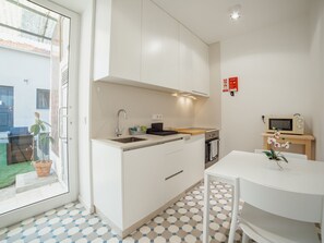 A compact kitchen with white cabinets, a sink, a microwave, and a small oven. There is a dining table with chairs and a potted plant. - Apartment  by Interhome (Porto)
