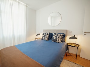 A bedroom with a bed, two bedside tables, a round mirror, and a window with curtains. - Apartment  by Interhome (Porto)