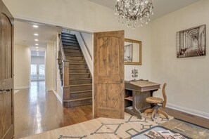 A hallway with a wooden door, a staircase, a chandelier, and a framed picture on the wall.