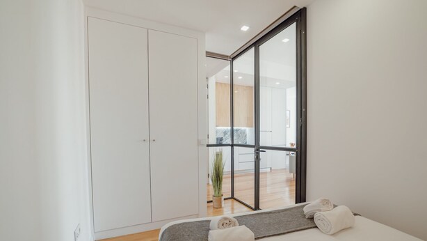 Quarto moderno com cama, guarda-roupa e porta de vidro deslizante para um banheiro.