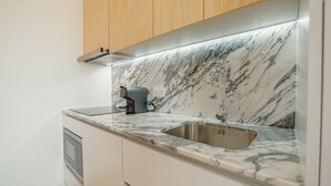 Cozinha com bancada de mármore, pia de aço inoxidável e armários de madeira.