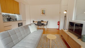 Un soggiorno moderno con divano, un tavolino rotondo, televisione e angolo cottura con piano in marmo.