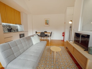 Ein modernes Wohnzimmer mit einer Couch, einem kleinen runden Tisch, einem Fernseher und einer Küchenzeile mit Marmorarbeitsplatte.