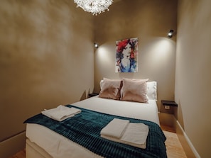 A bedroom with a bed, pillows, a blanket, a painting on the wall, and a light fixture. - Apartment  by Interhome (Porto)