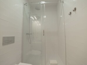 A glass-enclosed shower stall with a handheld showerhead, a wall-mounted towel dispenser, and a small towel on the floor. - Apartment  by Interhome (Porto)