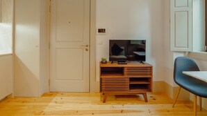 A room with a wooden floor, a television on a wooden stand, a door, and a chair. - Apartment  by Interhome (Porto)