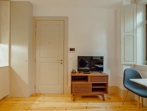 A room with a wooden floor, a television on a wooden stand, a door, and a chair. - Apartment  by Interhome (Porto)