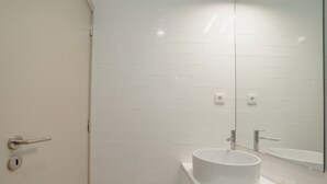 A bathroom with white tiled walls, a round sink, and a mirror. - Apartment  by Interhome (Porto)