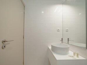 A bathroom with white tiled walls, a round sink, and a mirror. - Apartment  by Interhome (Porto)