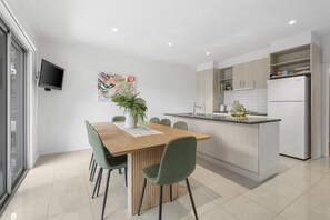 Eine moderne Küche mit Kochinsel, einem Essbereich mit Holztisch und grünen Stühlen sowie einem an der Wand befestigten Fernseher.