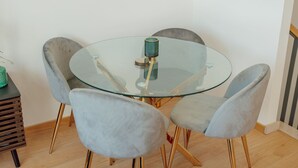 Een ronde glazen tafel met vier grijze bekleden stoelen, een groen cilindrisch object op de tafel, en een houten bijzettafeltje met een groen object erop.