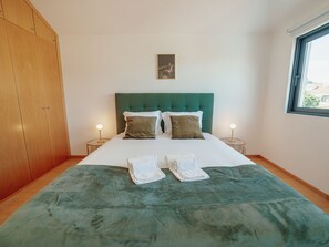 Ein Hotelzimmer mit einem Bett, zwei Nachttischlampen, einem grünen Kopfteil und einem Fenster.