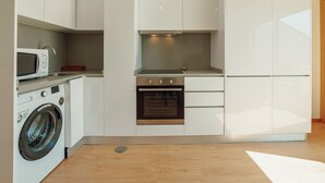 Een kleine keuken met een wasmachine, magnetron, oven en witte kasten.
