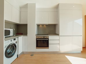 Eine kompakte Küche mit Waschmaschine, Mikrowelle, Backofen und weißen Schränken.