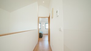 Een smalle gang met houten vloeren die leidt naar een kamer met een bed en een raam.