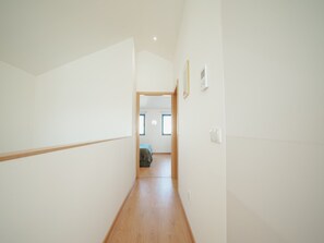 Ein schmaler Korridor mit Holzdielen führt zu einem Zimmer mit Bett und Fenster.