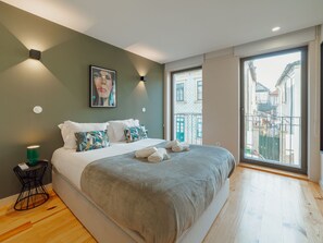 A modern bedroom with a large bed, a bedside table, a wall-mounted light, and a city view through the window. - Apartment  by Interhome (Porto)