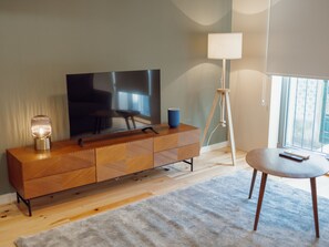A modern living room with a flat-screen TV, a wooden cabinet, a lamp, and a round table. - Apartment  by Interhome (Porto)
