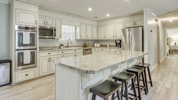 A spacious kitchen with white cabinetry, a large island with bar stools, stainless steel appliances, and a window providing natural light. - Shoals Area Oasis w/ Boat Dock & Outdoor Kitchen (Florence)