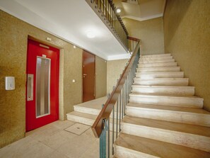 Un escalier avec une rampe en bois et des marches de couleur beige, menant à une porte rouge dotée d’un panneau de verre.