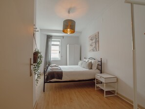 A bedroom with a bed, bedside table, hanging plant, window, and a wall-mounted artwork. - Apartment  by Interhome (Porto)