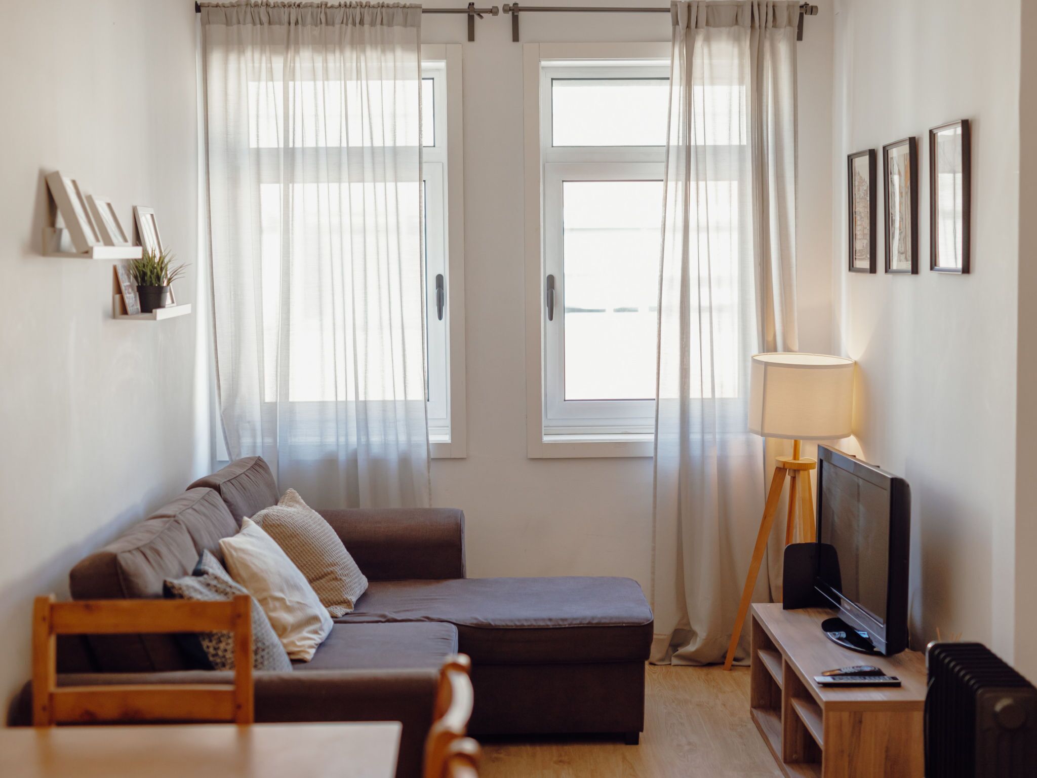 Uma sala de estar moderna com um sofá, uma televisão, um abajur e uma janela com cortinas.