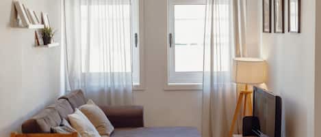 En moderne stue med en sofa, et fjernsyn, en lampe og et vindue med gardiner.