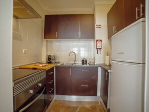 A compact kitchen with dark wooden cabinets, a stainless steel oven, a white refrigerator, and a tiled backsplash. - Apartment  by Interhome (Porto)