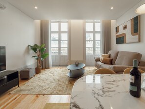 A modern living room with a sofa, a coffee table, a TV, and a large window with a view of buildings. - Apartment  by Interhome (Porto)
