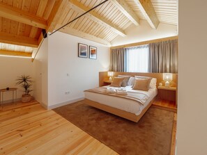A bedroom with a large bed, wooden ceiling beams, a small table, and a potted plant. - Apartment  by Interhome (Porto)