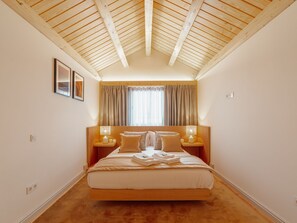 A bedroom with a sloped ceiling, a large bed, two bedside tables with lamps, a window with curtains, and framed pictures on the wall. - Apartment  by Interhome (Porto)