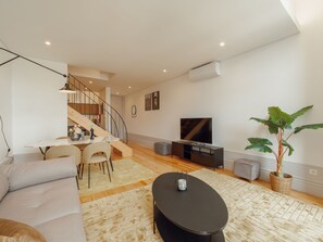 A modern living room with a sofa, a dining table, a staircase, a TV, and a potted plant. - Apartment  by Interhome (Porto)