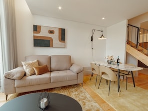 A modern living room with a sofa, a dining table with chairs, a coffee table, a floor lamp, and a staircase. - Apartment  by Interhome (Porto)