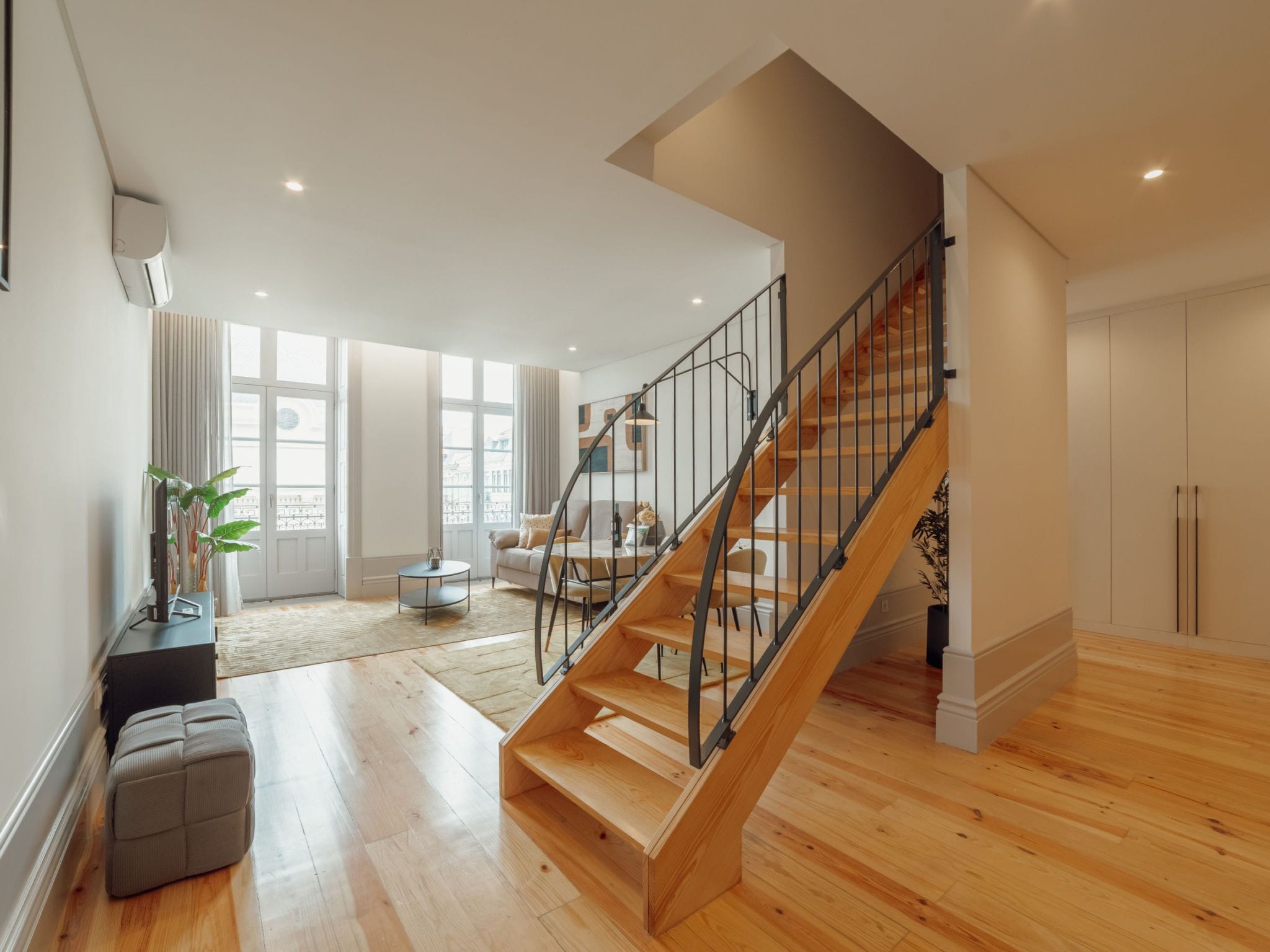 A spacious living area with a wooden staircase and a view of the city through large windows.