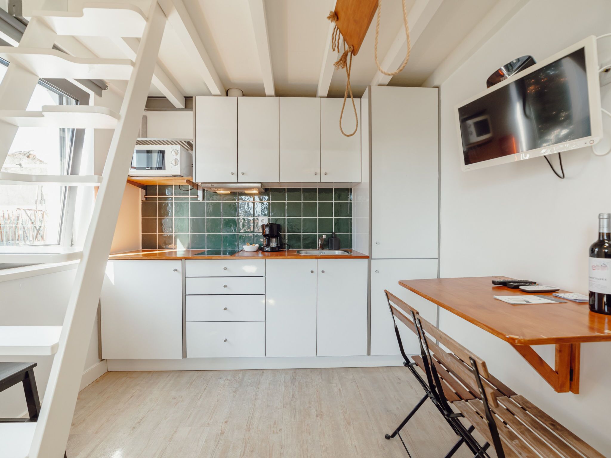A modern kitchen with white cabinets, a wooden table, and a built-in TV.