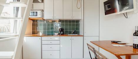 Una cocina moderna con armarios blancos, una mesa de madera y un televisor empotrado.