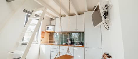 A modern kitchen with a loft bedroom, a hanging chair, and a desk with a computer.