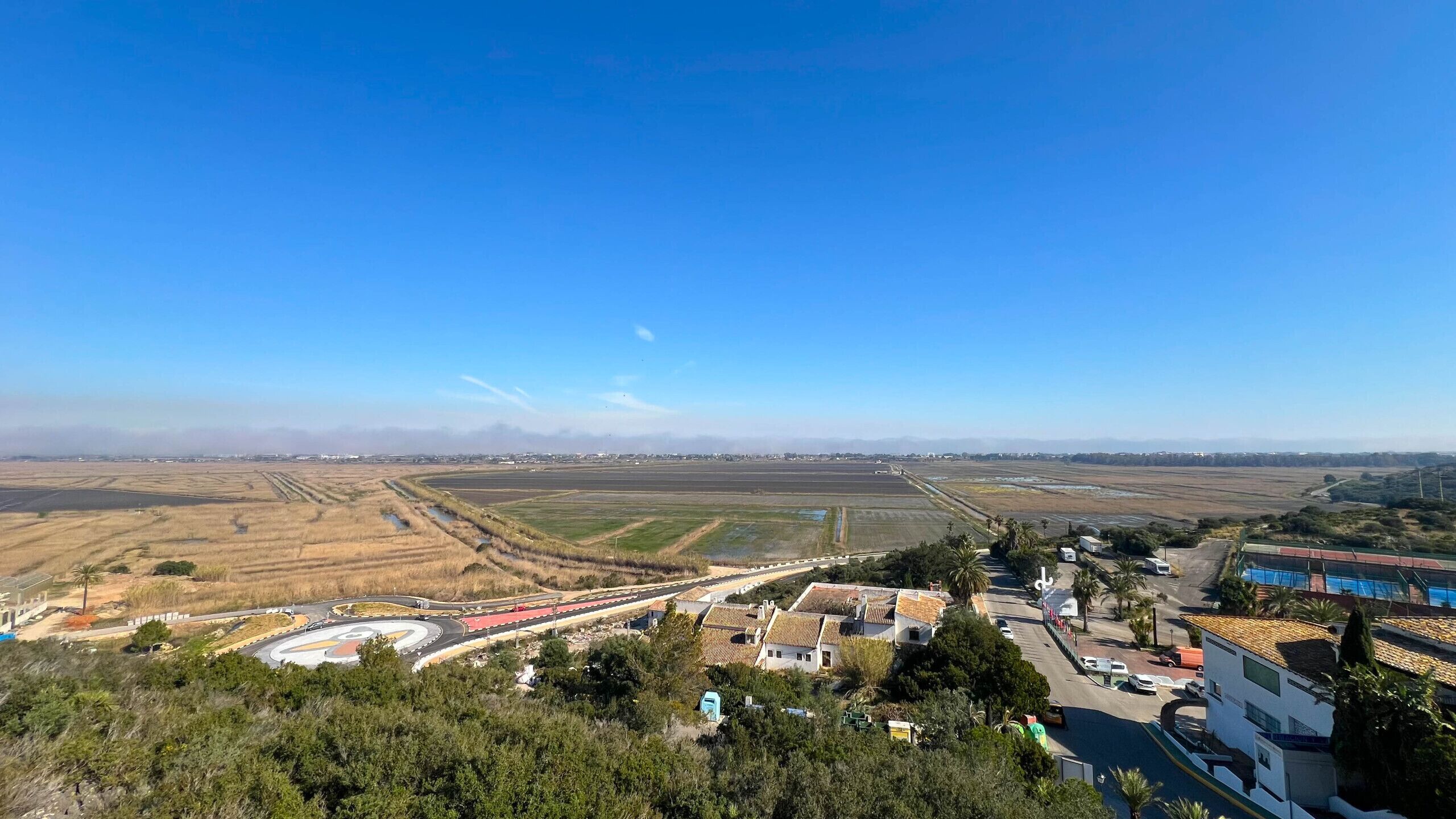 Ländliche Landschaft mit Feldern, einer gewundenen Straße und Gebäuden im traditionellen Stil.