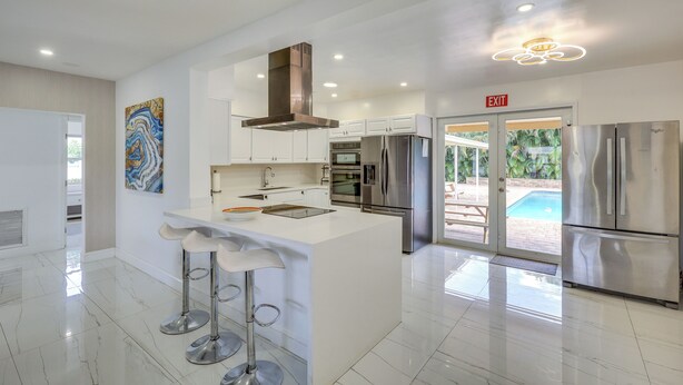 A modern kitchen with white cabinetry, stainless steel appliances, and a central island with bar stools. - Luxe Ft Lauderdale Pool Oasis Near Airport & Beach (Fort Lauderdale)