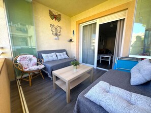 Ein Balkon mit einer Couch, einem Sessel, einem Tisch und einer Schiebetür zum Schlafzimmer.