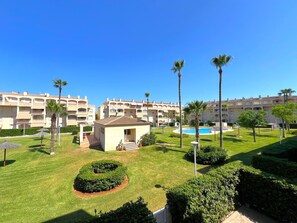 Ein Hotelinnenhof mit Schwimmbad, Palmen und gepflegten Rasenflächen.
