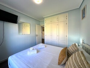 Ein Schlafzimmer mit einem Bett, einem an der Wand befestigten Fernseher und einem Kleiderschrank.