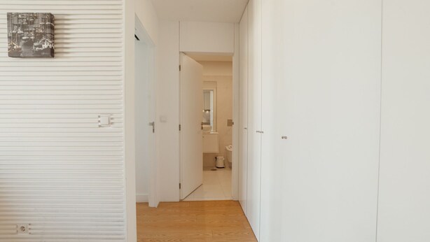 Un pasillo con suelo de madera, paredes blancas y una puerta que da a un baño.