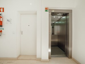 Ein Aufzug mit metallischer Innenausstattung und einer weißen Tür, über ihr befindet sich ein kleines Schild.